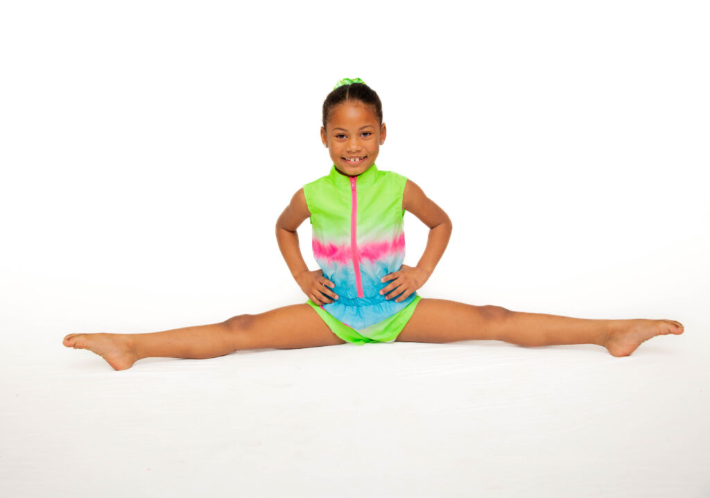 Young girl in a colorful outfit doing a split on the floor.
