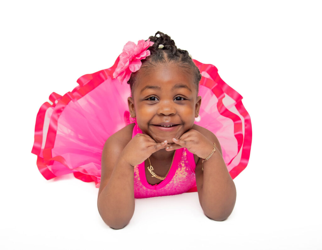 Smiling toddler girl in a bright pink dress lying on her stomach.